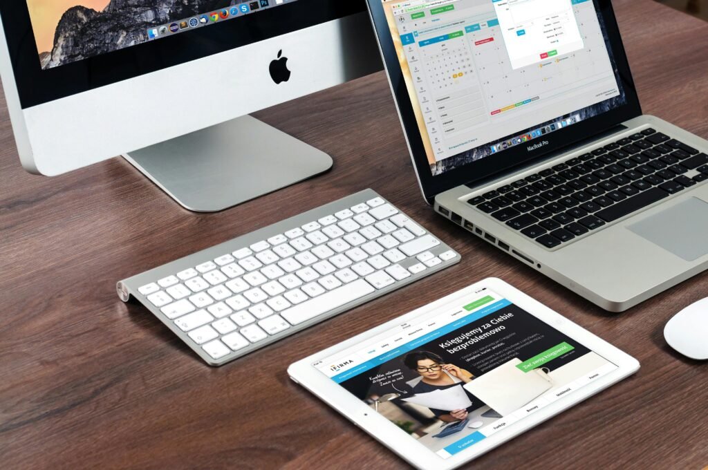 A desktop computer, a laptop and a tablet on a wooden desk, with websites open on all three screens